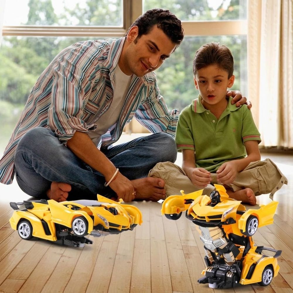 A man and a young boy sit on a wooden floor in front of a large window, playing with two yellow toy cars that transform into robot figures. The toys are bright yellow with black and silver details.